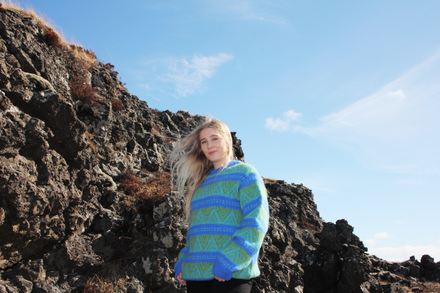Person wearing a blue and green patterned sweater standing on rocky terrain with a clear sky.