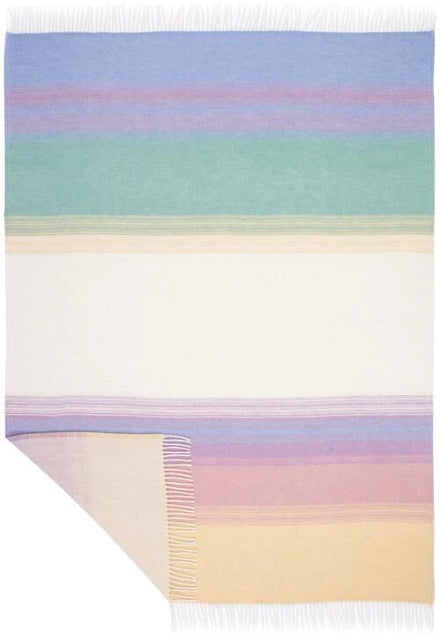 A rectangular woven throw blanket with horizontal pastel stripes in blue, purple, green, cream, pink, and yellow, finished with white fringe on two short ends and one corner turned down to show texture.