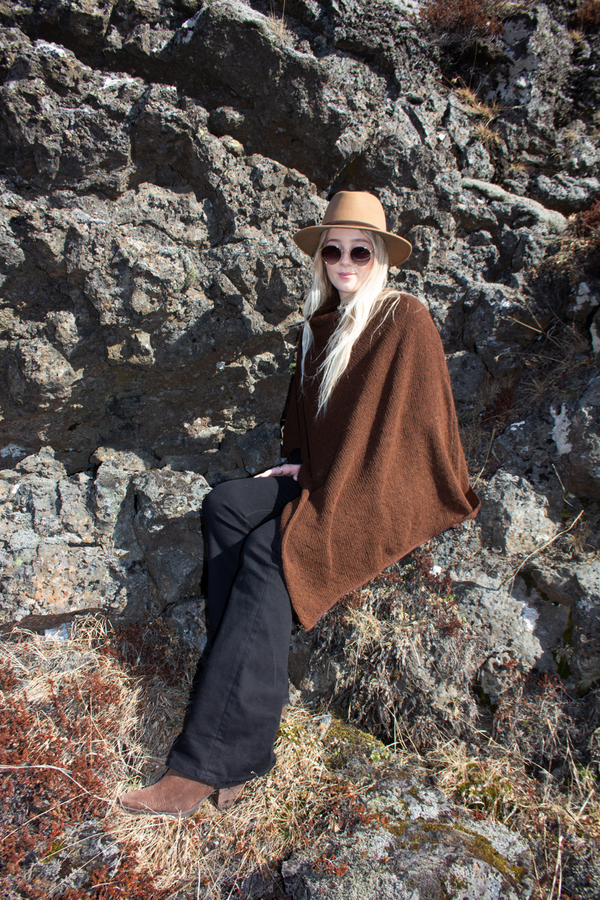 woman sitting in the lava field dressed in poncho and hat