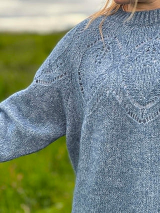 Close-up of a blue knitted sweater with intricate patterns on a blurred green background