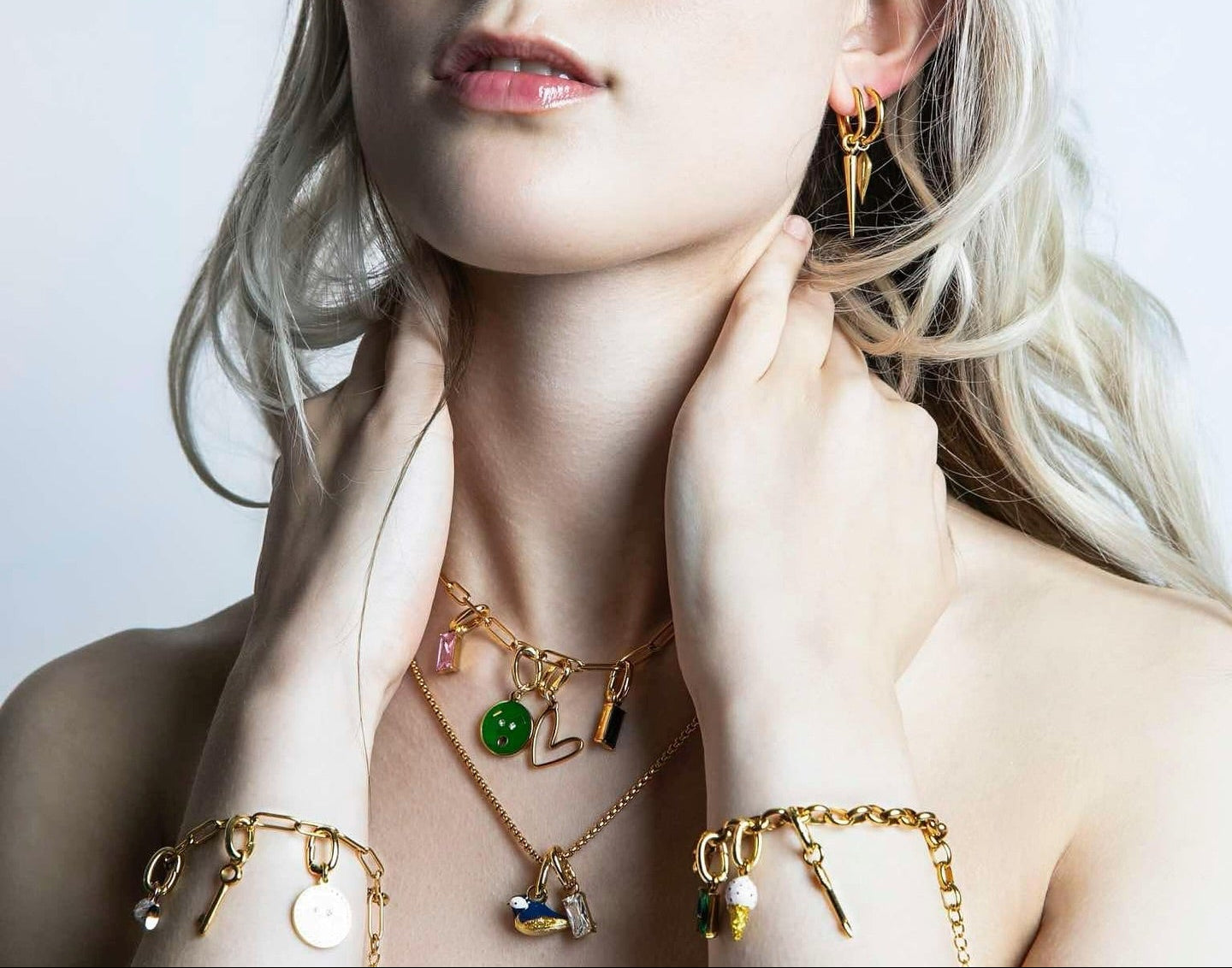 Woman wearing gold jewelry with various charms against a light background