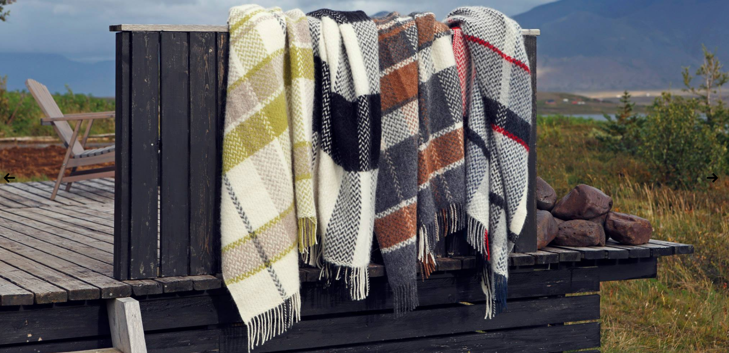Plaid icelandic blankets draped over a wooden structure with a scenic background
