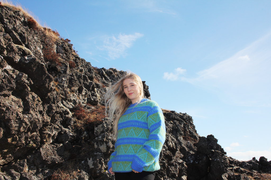 Person wearing a blue and green patterned sweater standing on rocky terrain with a clear sky.