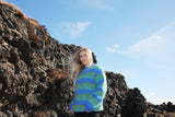 Person wearing a blue and green patterned sweater standing on rocky terrain with a clear sky.