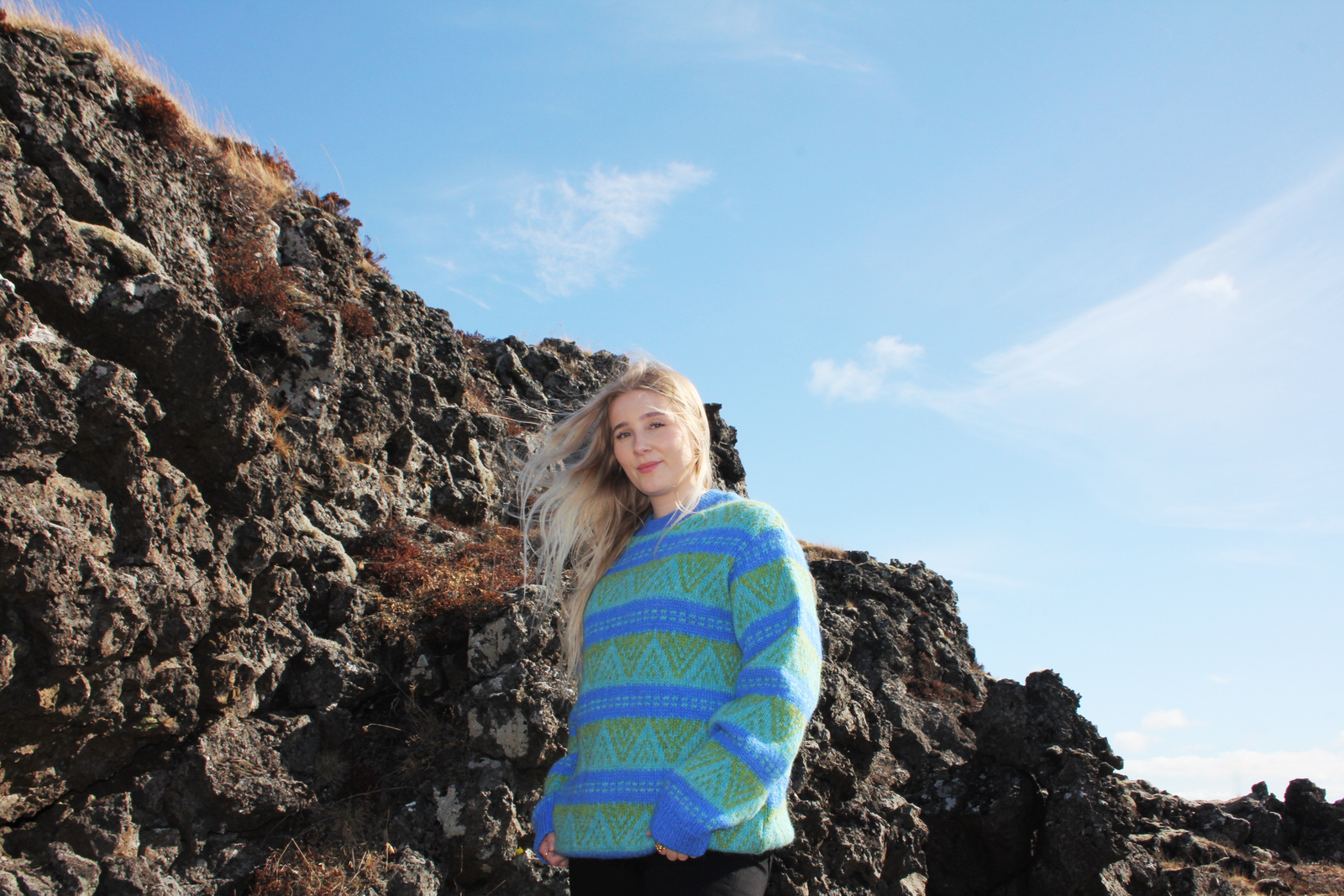 Person wearing a blue and green patterned sweater standing on rocky terrain with a clear sky.