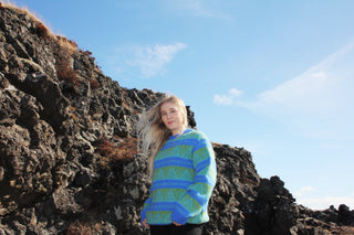 Person wearing a blue and green patterned sweater standing on rocky terrain with a clear sky.
